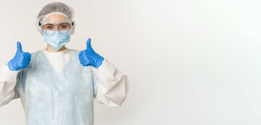 Portrait of doctor in personal protective equipment, showing thumbs up, wearing face mask, concept of covid-19 and pandemic, white background.