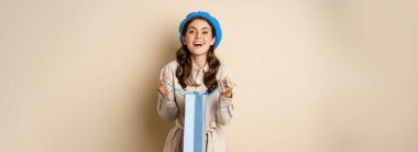 Mutlu genç kadın gülümsüyor, hediye paketini açıyor ve gülüyor, hediye veriyor, bej arka planda duruyor..