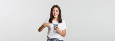 Heyecanlı ve mutlu esmer kız akıllı telefon ekranını işaret ediyor..
