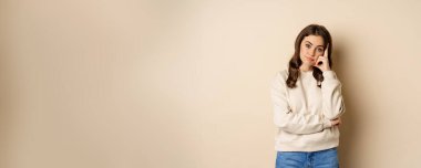 Annoyed woman, roll eyes and looking unamused, bothered and bored, standing over beige background.