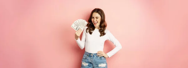魅力的な若い女性はピンクの背景の上に立って 手にお金 ローン マイクロクレジットとショッピングの概念を保持する スペースのコピー — ストック写真