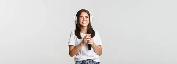 魅力的な笑顔ブルネットの女の子でヘッドフォンで カラオケを歌い マイクを保持 — ストック写真