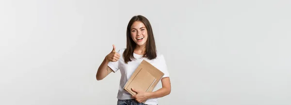 Χαρούμενα Χαμογελαστό Κορίτσι Κρατώντας Σημειωματάρια Και Δείχνει Αντίχειρες Προτείνουμε Μαθήματα — Φωτογραφία Αρχείου