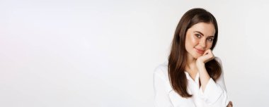 Close up of beautiful, coquettish brunette woman, blushing and smiling flirty, posing against white background. Copy space