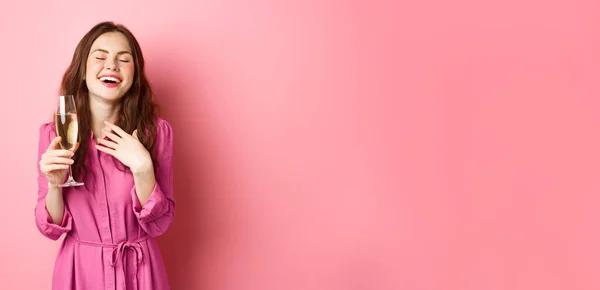 stock image Celebration and holidays concept. Stylish coquettish woman in trendy dress, holding glass of champagne at party, smiling pleased, standing over pink background.