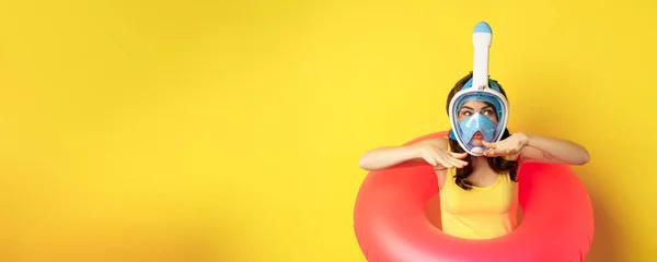 stock image Beautiful girl in diving mask, going snorkling, wearing swimming ring, showing swim motion, standing over yellow background.