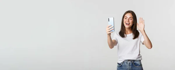 友善迷人的女孩打招呼 在视频通话时与智能手机挥手 — 图库照片