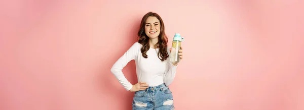 健康的なライフスタイル 幸せな笑顔の女性はレモンと水のボトルを保持します ビタミンCを飲む カメラを見て喜び ピンクの背景に対してポーズ — ストック写真
