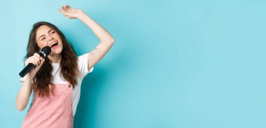 Güzel bayan şarkıcı mikrofon tutuyor, mikrofonda karaoke söylüyor, mavi arka planda duruyor..