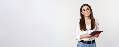 Smiling modern woman standing with digital tablet, laughing and looking happy, working, posing against white studio background.