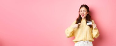 Esmer, beyaz bir kızın plastik kredi kartını işaret eden portresi, bankayı tavsiye eden, alışverişe devam eden, pembe arka planda duran.