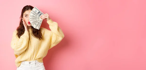有魅力的女模特 带着钱 半张着钞票 摸着脸 吻着嘴唇 站在粉色的背景下 — 图库照片