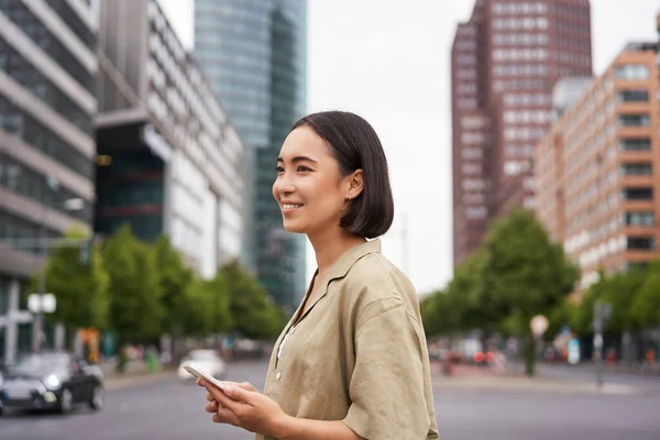 若いアジアの女性は スマートフォンアプリで街を探索し 携帯電話を保持し スクリート上を歩く — ストック写真