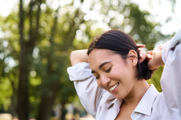 stock image Beautiful young woman tying her hair while walking in park, smiling romantic, enjoying warm day.
