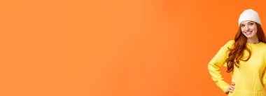 Modern hippi kız kış tatillerinde arkadaşlarıyla kartopu oynuyor. Barış işareti olarak kardan adamın yanında poz veriyor. Turuncu arka planda beyaz bere ve süveter giyiyor..