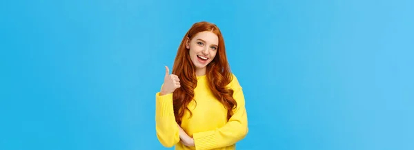 好主意 可爱可爱的红头发女友鼓励你去尝试 认可好的选择 高兴地微笑 点头认可 像大拇指一样做手势 站在蓝色的背景上 — 图库照片