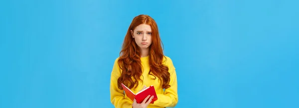 動揺と不安 黄色のセーターの悲しいかわいい赤毛の女の子 眉をひそめ カメラを見て落ち込んで 赤のノートブックを保持し 誰かの日記を読んで 紙の上で考えを共有し 悩んで — ストック写真