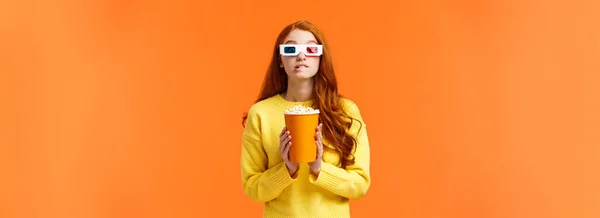 stock image Lifestyle, hobby and people concept. Cute geeky redhead woman in 3d paper glasses, holding popcorn and biting lip as staring at favorite actor playing in movie, visit cinema to watch premiere.