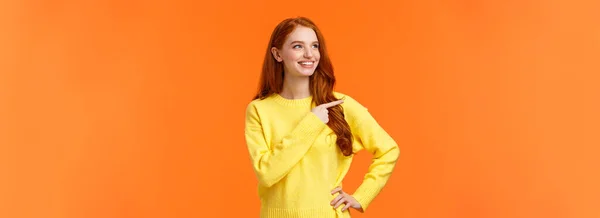 夢のような 活気に満ちた良い黄色のセーターの赤毛の女性は 優れた休日の贈り物を発見し 消費者の左を指して 満足して見て ピッキング製品として笑みを浮かべて 意思決定 オレンジの背景 — ストック写真