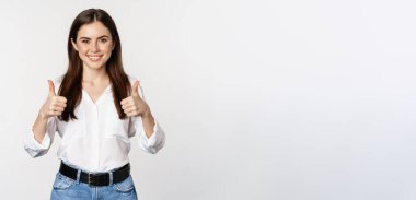 Happy smiling girl showing thumbs up, student with satisfied feedback, recommending smth, standing over white background.