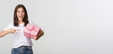 Şaşırmış mutlu genç bir kadın gülümsüyor ve hediye paketini işaret ediyor..