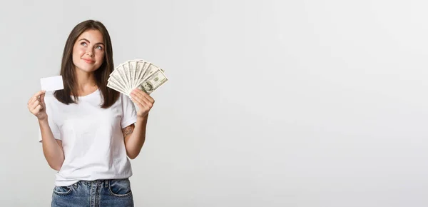 Στοχαστικό Χαμογελαστό Κορίτσι Κρατώντας Χρήματα Και Πιστωτική Κάρτα Κοιτάζοντας Πάνω — Φωτογραφία Αρχείου