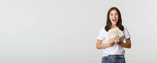 Happy attractive brunette girl holding money and smiling excited, white background.