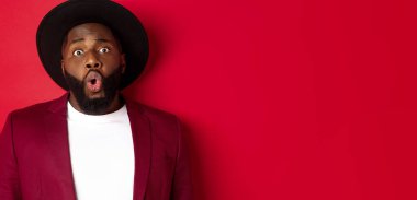 Şaşkın bir şekilde kameraya bakan, kırmızı arka planda duran siyahi adamın yakın çekimi..