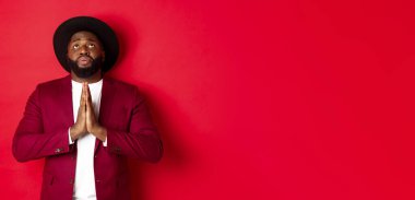 Umutlu ve üzgün siyahi adam Tanrı 'yla konuşuyor, dua ediyor, yukarı bakıyor, yalvarıyor, yardım dileniyor, kırmızı arka planda duruyor..