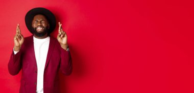 Umut dolu Afrikalı Amerikalı bir adam dilek tutuyor, şans diliyor ve iyimser gülümsüyor, kırmızı parti geçmişine karşı duruyor..