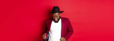 Noel ve insanlar kavramı. Mutlu siyah adam yeni yılı kutluyor ve dans ediyor, parti kıyafeti giyiyor, kırmızı arka plan.