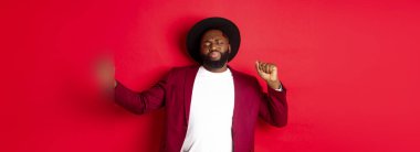 Noel ve insanlar kavramı. Mutlu siyah adam yeni yılı kutluyor ve dans ediyor, parti kıyafeti giyiyor, kırmızı arka plan.