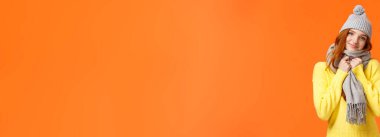 Sevecen, güzel, kızıl saçlı, rahat ve sıcak bir kadın, sevgililer günü hediyesi, sevimli bir şapka ve güzel bir eşarp, yana yatmış, gülümseyen kamera neşeli, ayakta duran, coşkulu ve mutlu bir turuncu arka plan..