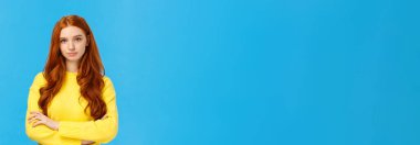 Profesyonellik, e-ticaret ve iş konsepti. Ciddi görünüşlü, kararlı, sarışın, sarı kazaklı, kolları çapraz göğüslü, kendine güvenen, kameraya bakan, mavi arka planda bir kadın..