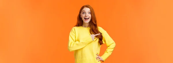 アップビートと夢のようなかわいい赤毛の女性は 海外旅行のチャンスを得ました 素晴らしい会社について話して 販売で製品を促進します 魅力的なカメラの笑顔を見つめ 左を指して オレンジの背景 — ストック写真