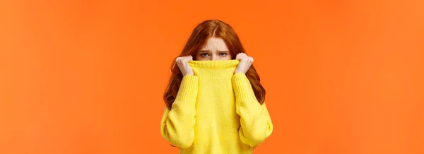 かわいい臆病な優しい赤毛の女の子は寒い天気を嫌う 十代の若者は 満足していない 失望や孤独を見て 鼻の上にセーターを引っ張ったり カメラを見て顔をしかめる オレンジの背景 — ストック写真