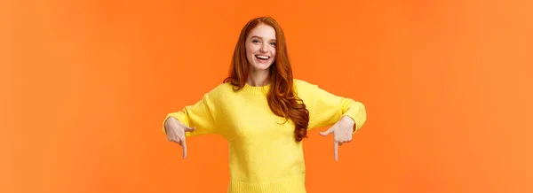 ウエストアップの肖像画明るい赤頭の女性学生黄色のセーターで チェックアウトイベントを招待し 誇りをお勧めします クリスマス販売 休日のプロモーション ポインティングと笑顔 オレンジの背景 — ストック写真