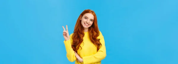 ウエストアップは黄色のセーターで陽気でかわいい赤毛の現代的な女性を撮影 傾きの頭と笑顔素敵な 平和の兆候を示す 肯定的な感情を表現 喜びと幸福 青の背景 — ストック写真