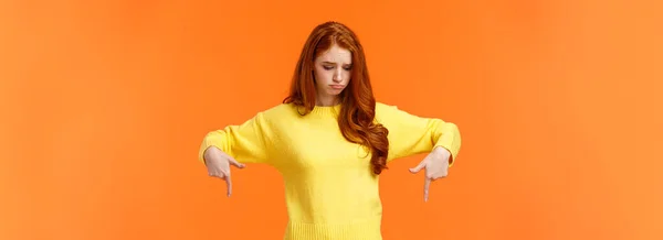 穿着黄色毛衣的嫉妒 悲伤和闷闷不乐的红头发女人 带着嫉妒或失望的心情朝下看 感到嫉妒和后悔错过了机会 站在橙色的背景下 — 图库照片