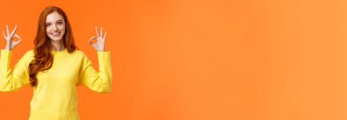 Kabul etmek harika bir fikir. Sarı kazaklı güzel bir kızıl kız, tamam diyor, iyi ya da onay işareti gülümsüyor, onaylıyor, sonuçtan memnun, hepsi mükemmel, turuncu arka plan.