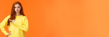 Kız üzgün ve tatminsiz görünüyor. Üzgün, somurtkan, solu kıskançlıkla gösteren kızıl saçlı kadın partiye gelemiyor, somurtuyor ve somurtuyor, istediğini gösteriyor, turuncu arka planda mutsuz duruyor..