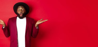 Noel alışverişi ve insanların konsepti. Yakışıklı afro-amerikan adam şaşırmış, ellerini yana açmış, tanıtım tekliflerini fotokopi alanında, kırmızı arka planda gösteriyor..