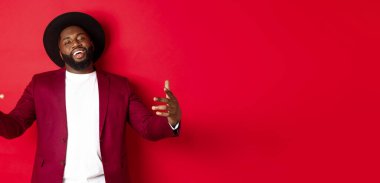 Noel alışverişi ve insanların konsepti. Kendine güvenen ve küstah bir adam jestle dans ediyor, hip hop yapıyor ve kamera karşısında kendinden emin, kırmızı arka planda..