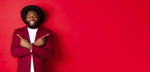 stock image Happy young man dreaming and pointing fingers sideways, close eyes and smiling, showing two things, standing over red background.