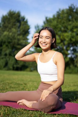 Meditasyon ve farkındalık. Genç Asyalı kadın parkta spor minderinde gülümsüyor, yoga eğitimi alıyor, temiz hava üzerinde meditasyon yapıyor..