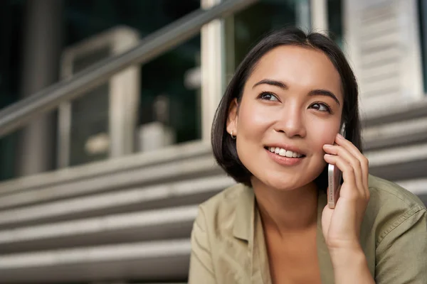아시아 소녀의 얼굴은 휴대폰으로 이야기하는 미소를 짓는다 여자가 친구에게 전화하고 — 스톡 사진