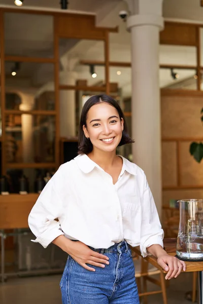 stock image Smiling asian manager, confident woman standing near restaurant entrance, cafe owner welcomes guests.