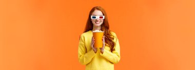Kız filmin başlamasını bekliyor, heyecanla gülümsüyor, sinemayı ziyaret ediyor, elinde patlamış mısır tutuyor ve sırıtıyor, yeni bir fantezi filmi izlemek için 3D gözlük takıyor, büyük ekranda galayı izlemek gibi, turuncu duvarda..