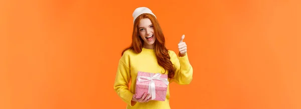 stock image Girl enjoying holidays, got super cool present. Cheerful and upbeat good-looking redhead woman in yellow sweater, winter white beanie, show thumb-up in yes, approval or like gesture, smiling.