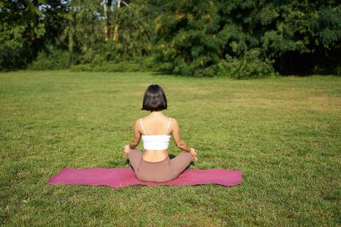 Kadın siluetinin yoga yapması, spor minderinde oturması ve yeşil çimlerde meditasyon yapması..